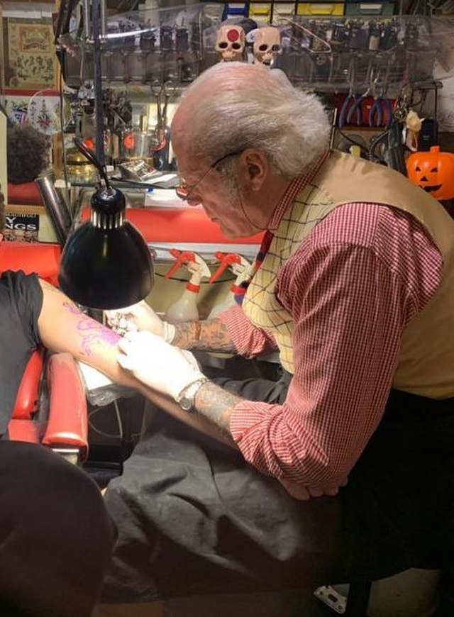 old guy tattooing someone in a chair